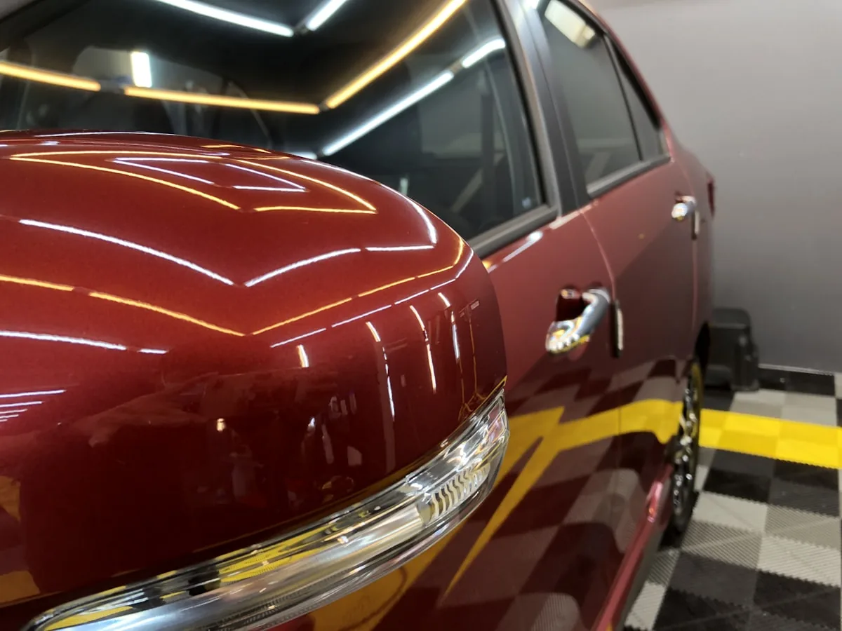 Lateral de carro vermelho encerado, com o retrovisor e a porta refletindo as luzes como espelho