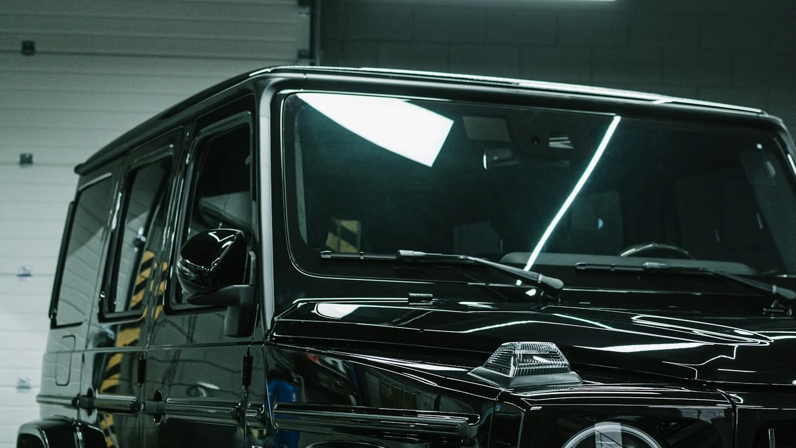 Carro preto brilhando dentro do box, com as luzes do teto refletidas na lataria