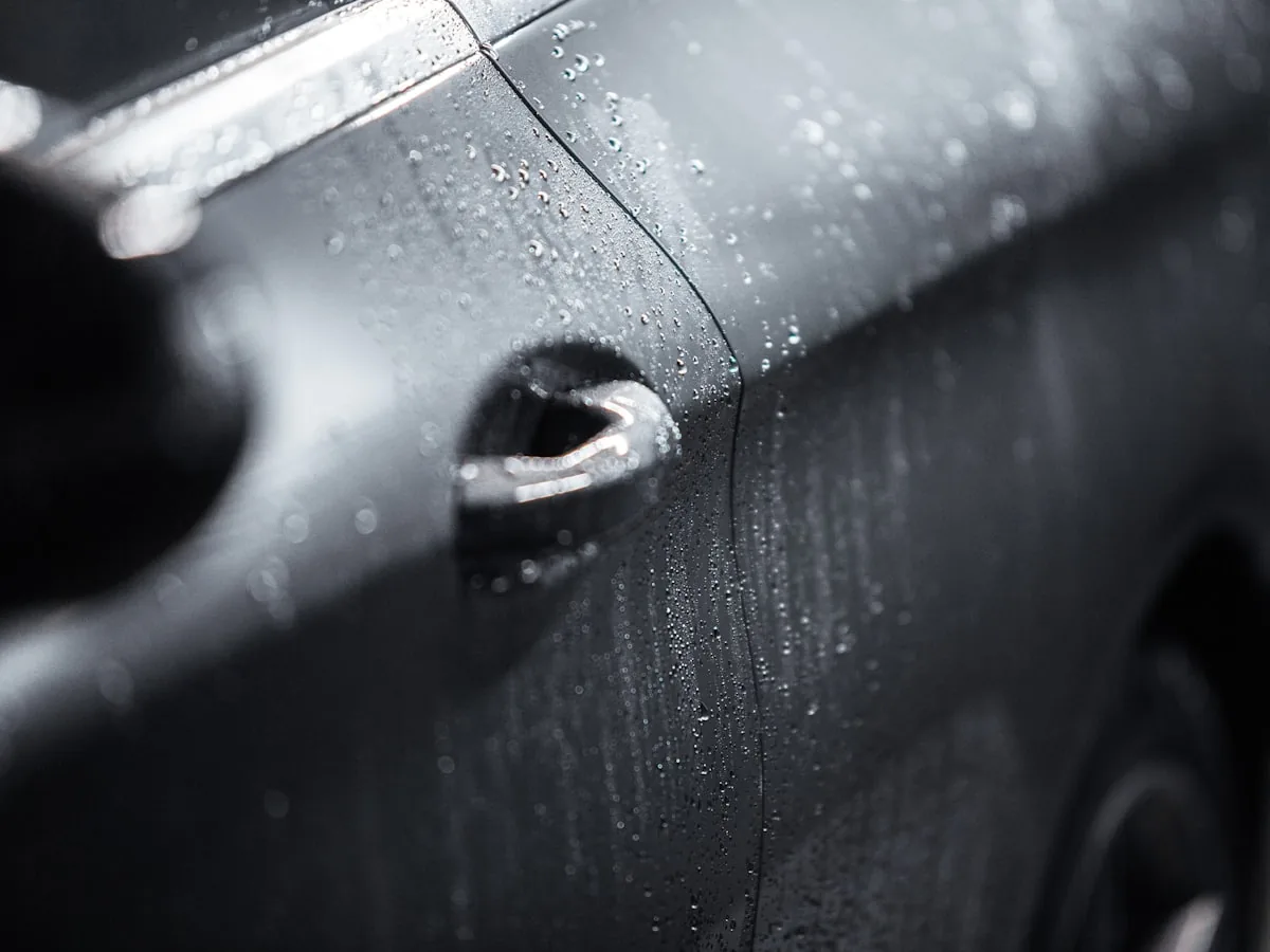 Gotas de água formadas na porta de um carro preto protegido com cera